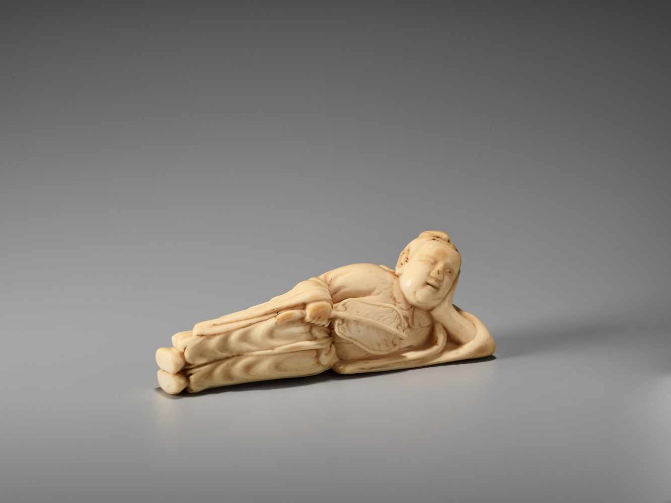 AN IVORY NETSUKE OF A RECLINING CHINESE IMMORTAL WITH A FANUnsigned, ivory netsukeJapan, late 18th - Image 4 of 6