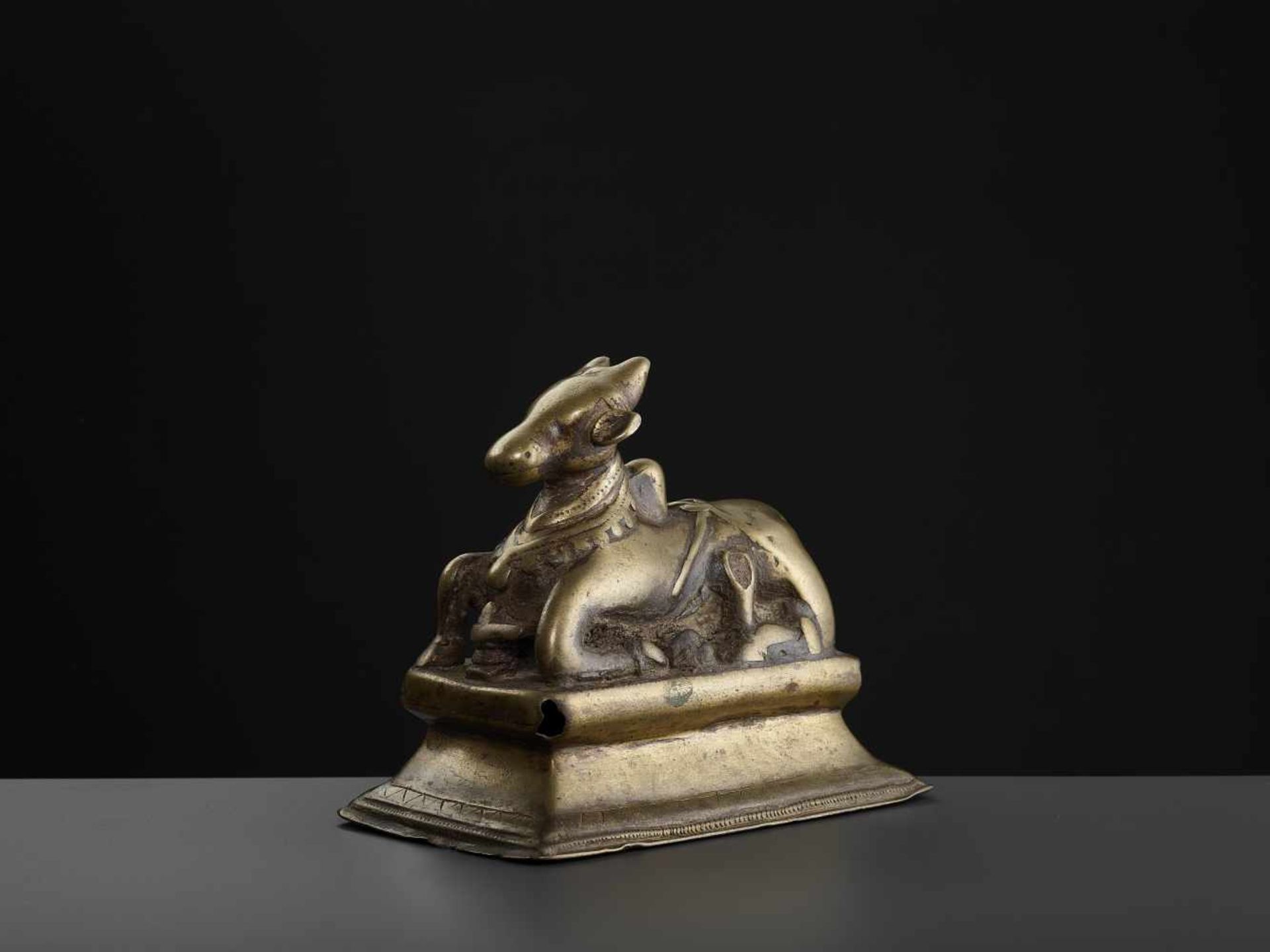 A BRASS NANDI 15TH CENTURYIndia, Himachal Pradesh. The divine cow reclining on a rectangular,