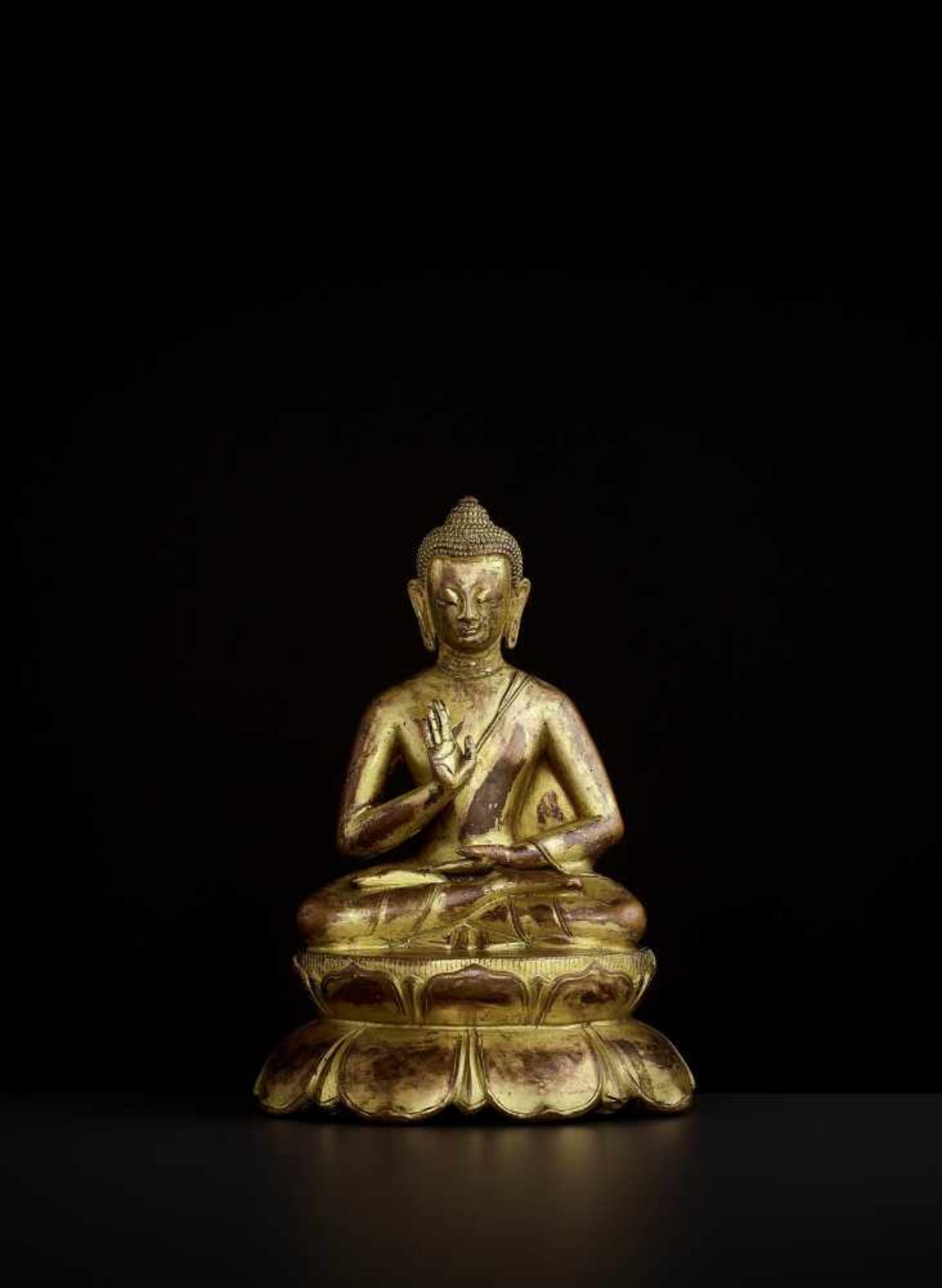 A BUDDHA AMOGHASIDDHI, NEPAL 17TH CENTURY The heavily cast gilt copper-alloy figure is seated in