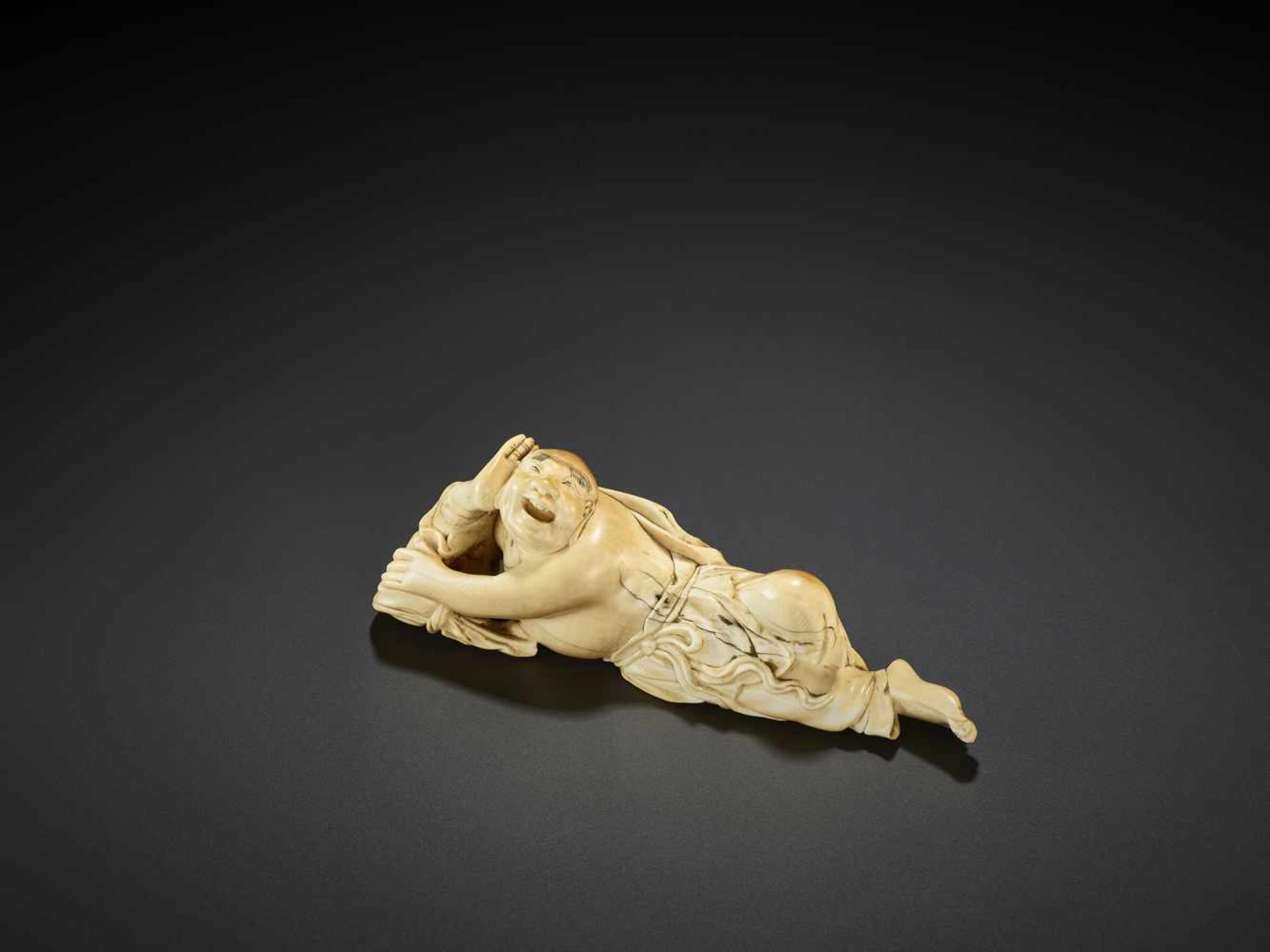 AN IVORY STATUE OF BUDAI, KANGXI China, 1662-1722. The laughing Buddha depicted in a reclining