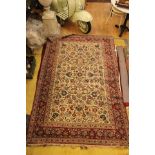 A medium sized hand knotted woollen rug, cream ground centre, stylised floral patterns, red border,