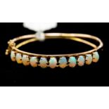 An opal and 14ct gold hinged bangle, comprising eleven white oval opals, displaying green, blue,