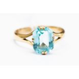 An unmarked yellow metal and paste set dress ring, with a blue rectangular cut stone, size Q,