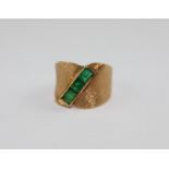 An 18ct. gold and emerald ring, c.1970's, in the cross-over style, having wide textured band set