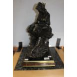 A bronzed sculpture of a fisher woman seated upon rocks,
