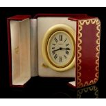 A Cartier alarm clock with circular white enamel dial, cream and gilt oval case with easel back,