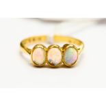 An opal ring, set with three oval rub-over set opals, set in 22ct gold, stamped, size O,