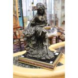 A bronzed sculpture of a fisher woman seated upon rocks,