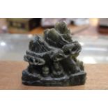 An early 20th Century green soapstone figure of a Buddha in a sitting position amongst trees,