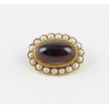A yellow metal, pearl and garnet brooch, of oval form, having central oval cabochon garnet surrouned