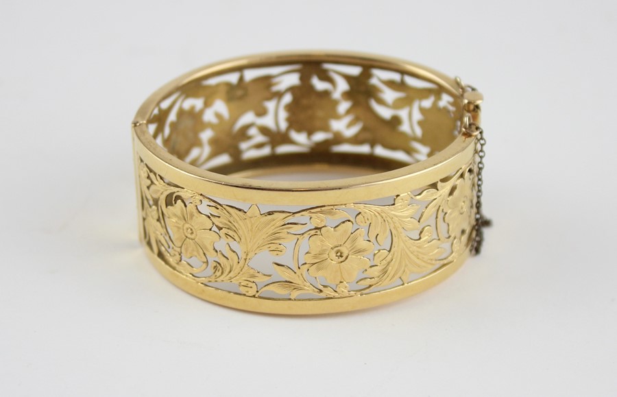 An 18ct. yellow gold pierced and hinged bangle, of typical ovoid form, each half having pierced