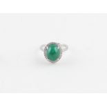 An 18ct. white gold, cabochon emerald and diamond halo style ring, four claw set central oval