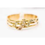 An unmarked yellow metal dress ring set with white stones in a snake like shape over three bars,