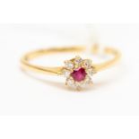 A ruby gold diamond small cluster ring, the central round ruby with a claw set diamond surround,