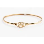 An unmarked 9ct gold bangle, open stylized circular detail to the top,