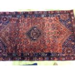 A 20th Century hand knotted woollen rug with geometric patterns on a red and blue ground.