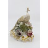 A Royal Crown Derby peacock standing on a gilded mound encrusted with various flowers with gilt,