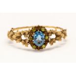 A 9ct gold hinged bangle with stone set cluster front, with leaf design decoration to the shoulders,