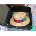 A straw boater hat with claret red and green ribbon and green bow round brim,