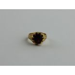 An 18ct. gold and garnet ring, claw set large oval cut garnet to centre, with floral engraved