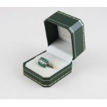 A white metal, diamond and emerald cluster ring, set row of five graduated round brilliant cut