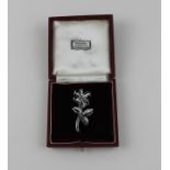 A white metal and diamond floral brooch, fashioned a six petal flower to stem with three leaves, the