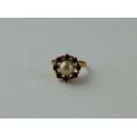 An 18ct. yellow gold, pearl and garnet ring, set central pearl surrounded border of eight claw set