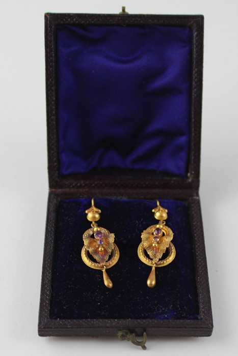 A cased pair of yellow metal and amethyst drop earrings, fashioned as two conjoined rings below a