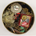 A collection of military cap badges and enamel lapel badges in a vintage CWS Biscuit tin to