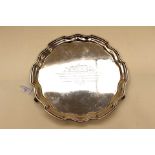 A George V silver salver, pie crust edge, raised on three scroll feet, presentation inscription,
