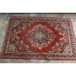 A hand knotted woollen rug with signs of wear. Red ground with navy, blue and cream floral design.