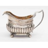 A late George III silver milk jug, gadroon border and fluted body, on four ball feet, Thomas Austin,