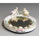 A Dresden porcelain framed mirror, encrusted with flowers and two cherubs holding a flower swag,