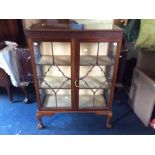 An early 20th Century two door glazed display cabinet, enclosing fitted shelves, with claw and