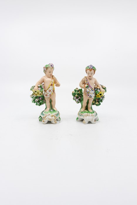 A pair of Derby cherubs, standing before bocage holding a basket, circa 1790, height 12cm (2)