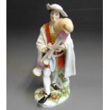 A Meissen figure of a Savoyard Bagpiper, dressed in a white cloak and breaches and a red coat,