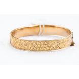 A 9ct gold hinged bangle, scroll decoration,