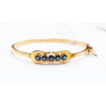 A yellow gold and sapphire hinged bangle, set with five round cut sapphires, tests as approx 14k,