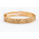 An unmarked 9ct gold bangle, hinged, floral engraved to top, weight approx. 18.6gms.