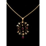 An Edwardian open work pendant set with seed pearls and red paste, floral accents on rope chain,