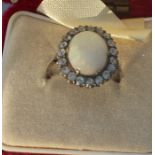 A white metal and opal ring, set oval cabochon precious white opal bordered by round cut clear