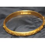 A Chinese yellow gold hinged bangle, of oval form, engraved with scrolling leaf design to the