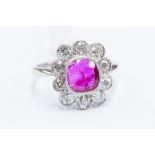 A ruby and diamond cluster ring, the cushion cut Burmese Ruby,  rub-over set with millegrain detail,