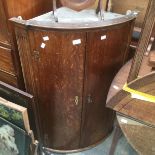 A George III oak bow fronted corner cupboard