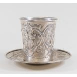 A silver beaker and saucer with embossed decoration