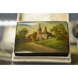 A Fedoskino Pegockuno Russian black lacquered papier mache box, the front depicting a church in a