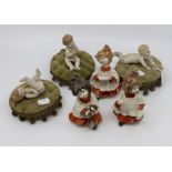 Three Capo Di Monte child choral singer statues and three continental porcelain babies on cushion