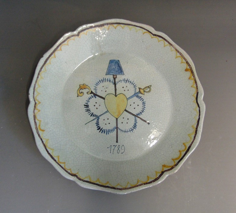 A faience armorial plate decorated with a heart and crossed swords, circa 1789, 24cm diameter
