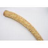 A worked and antique ivory tusk, circa 1910, extensively carved in high relief with beast-like