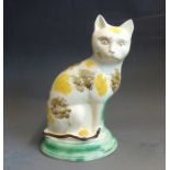 A Staffordshire pottery model of a cat with yellow and brown sponged decoration sitting on a green